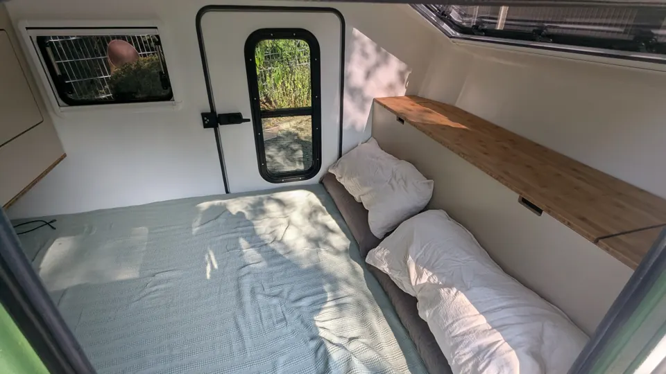 Bett mit Kissen, Bambusablage, Dachfenster und Tür mit Fenster im Innenraum