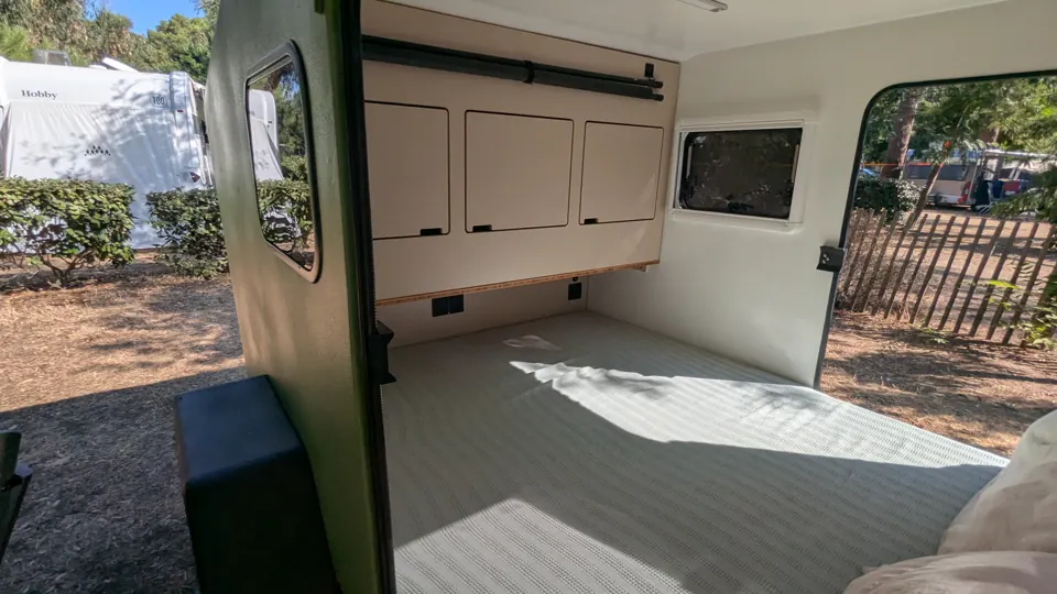 Blick durch die geöffnete Seitentür auf Bett und Einbauschrank