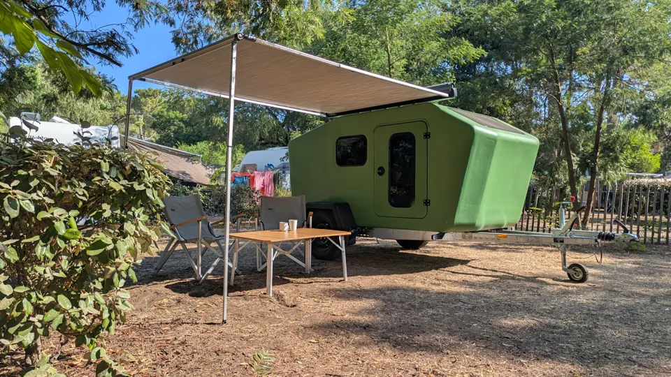 Grüner Glide mit Markise, Stühlen und Bambustisch auf einem sonnigen Campingplatz