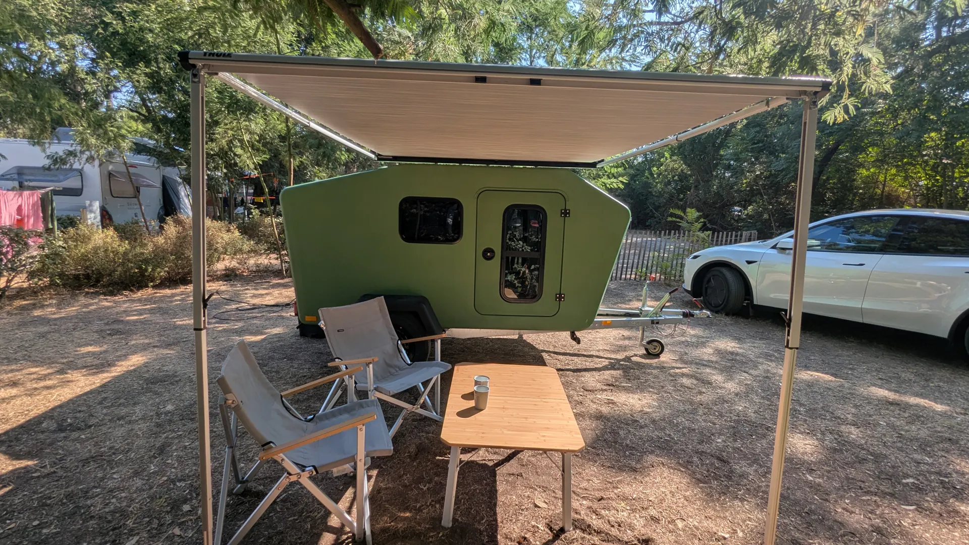 Ausgefahrene Markise über zwei Campingstühlen und einem Bambustisch vor dem grünen Glide auf einem Campingplatz
