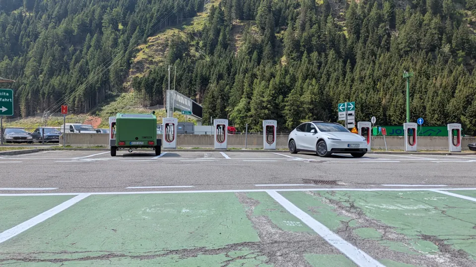 Glide und Tesla Model Y an einem Supercharger vor bewaldeten Bergen