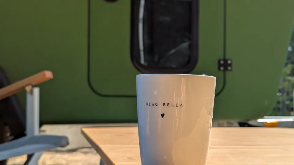 Kaffeebecher mit der Aufschrift Ciao Bella auf dem Bambustisch, dahinter die Tür des Glide