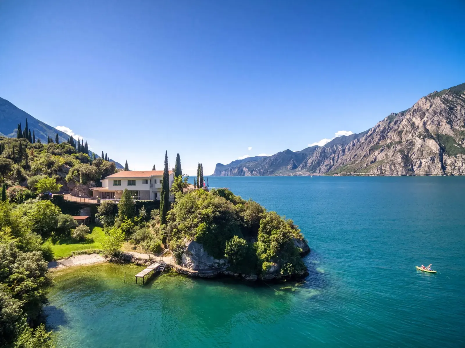 Tempesta am Nordostufer des Gardasees: Villa zwischen Zypressen über türkisem Wasser, dahinter die Berge
